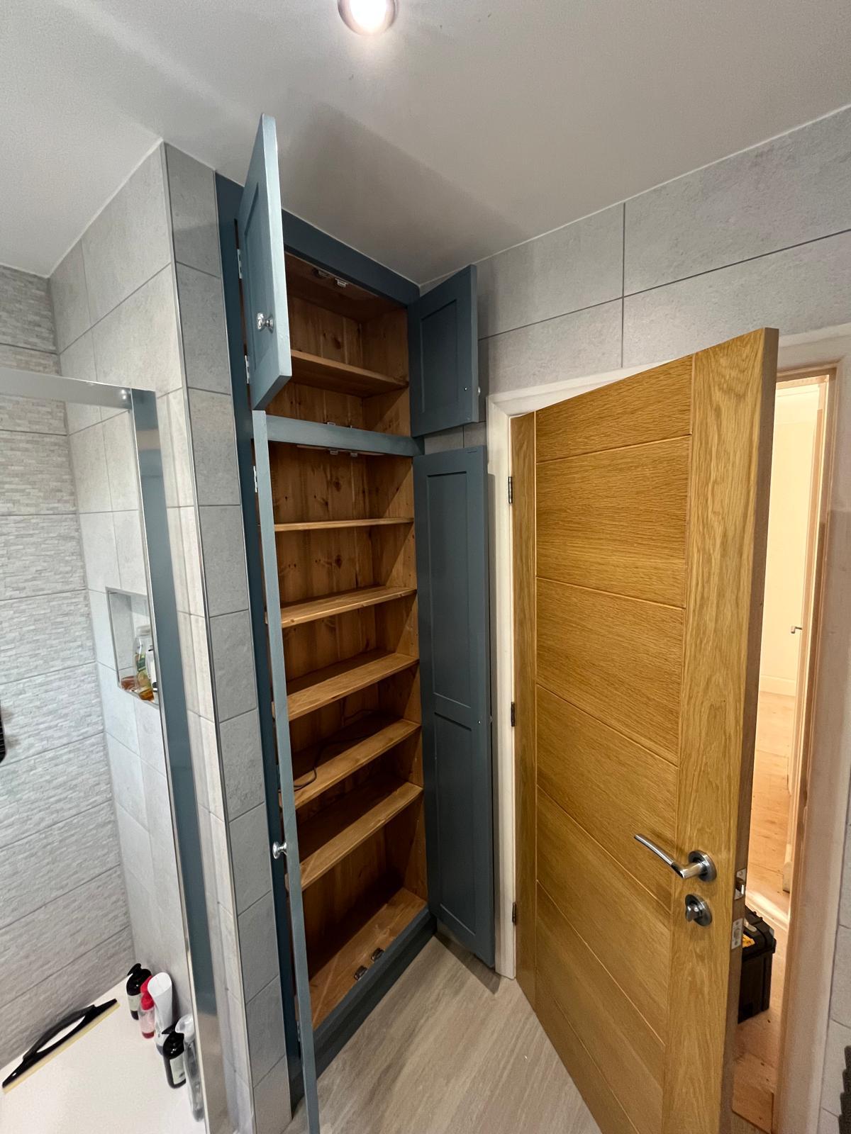 Open fitted bathroom cupboard showing wooden shelves