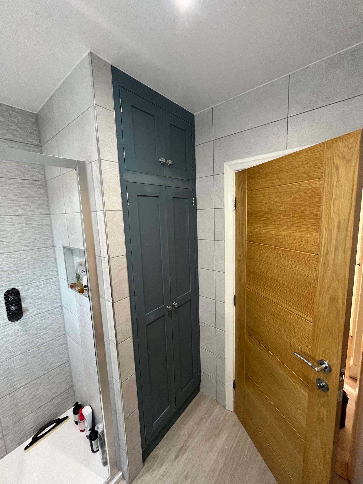 Tall dark painted fitted bathroom cupboard with panelled doors closed