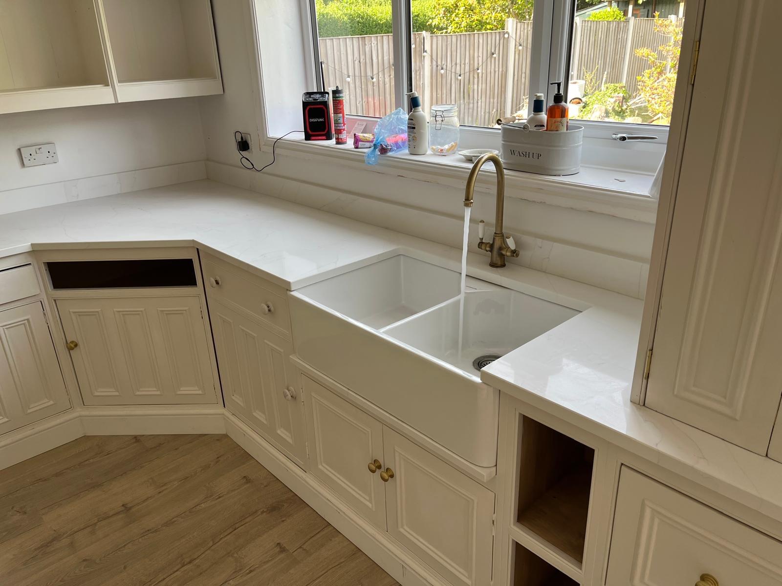 White double sink, brass-coloured tap and cream kitchen cabinets with white worktops